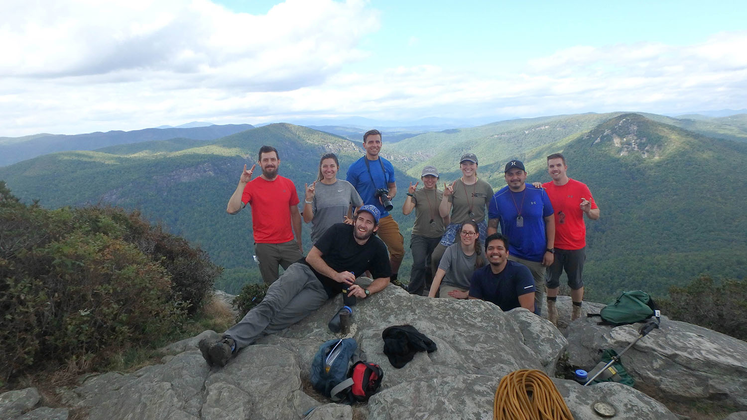 10 smiling people pose for a group photo on top of a mountain